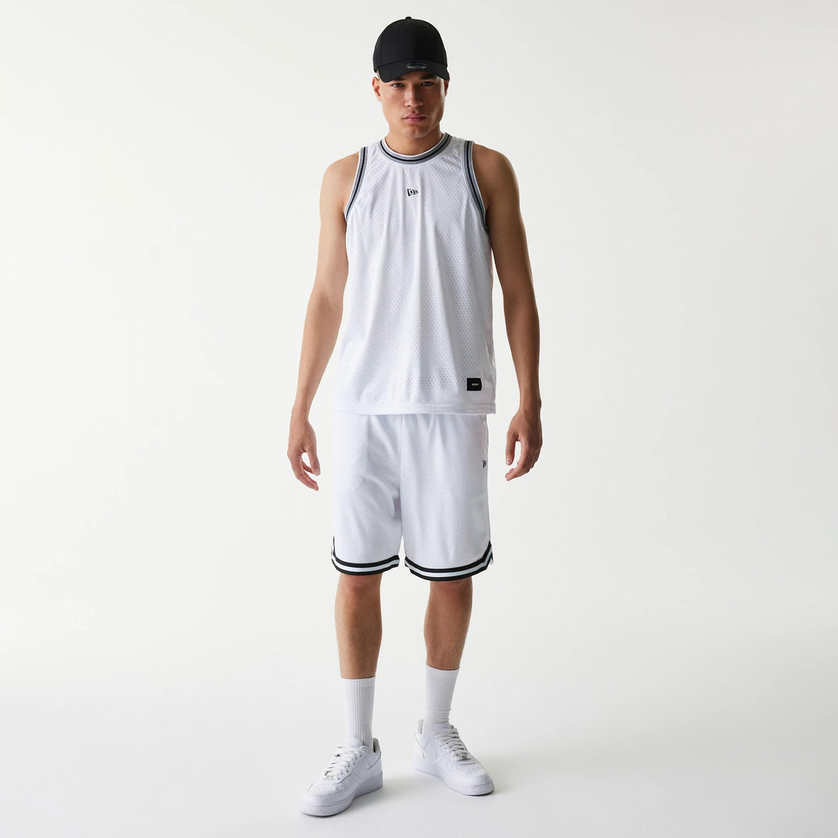New Era Japan Mesh White Shorts, on-model view featuring white shorts with a raised logo on the left leg hem, black trim detail along the edges, paired with a matching mesh top and a black cap.