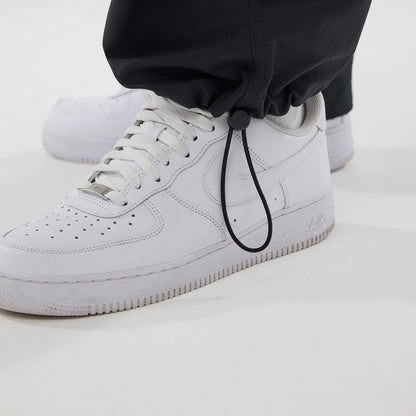 New Era NEC Logo Black Straight Leg Joggers, close-up showing adjustable elastic drawstring with toggle at the ankle cuff, paired with white trainers to highlight casual and sporty style.