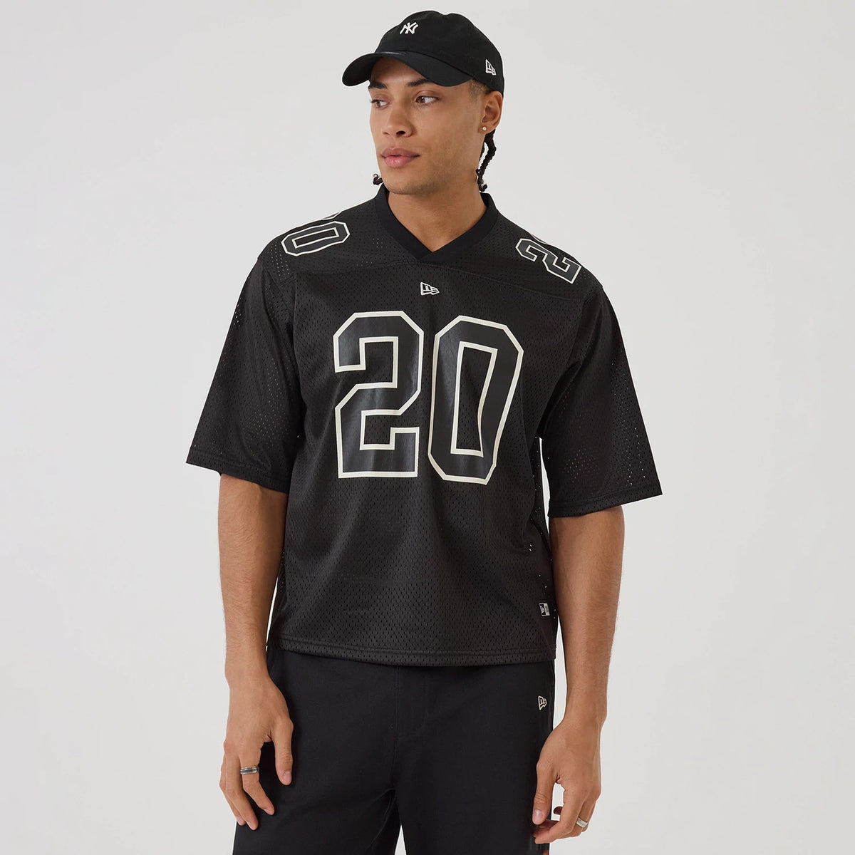 New Era Mesh Football Black Short Sleeve Shirt, front view on a model wearing a matching cap, featuring a large white number 20 on the chest, detailed sleeve numbers, and the New Era logo centred under the neckline.