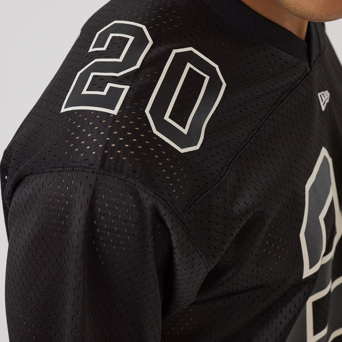 New Era Mesh Football Black Short Sleeve Shirt, close-up on a model showing the number 20 in white on the shoulder, with perforated mesh fabric and the New Era flag logo on the chest.