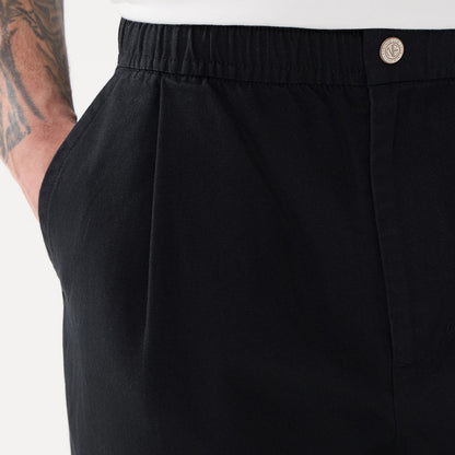 New Era Black Balloon Leg Trousers, close-up showing the elastic waistband with a button detail, side pocket, and a portion of the model's arm with a tattoo, highlighting the trousers' relaxed fit.