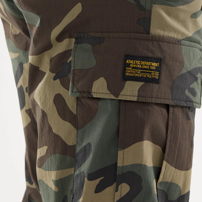 New Era Originators Woodland Camo Cargo Trousers, close-up showing the camo pattern on the cargo pocket with a black and yellow woven label reading “Athletic Department New Era Since 1920 Originators of the True Fitted”.