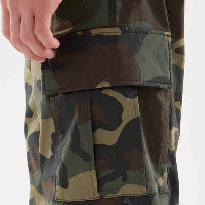 New Era Originators Woodland Camo Cargo Trousers, close-up view showing camouflage pattern with large pocket flap detail on the side of the trouser leg and a hand placed above the pocket.