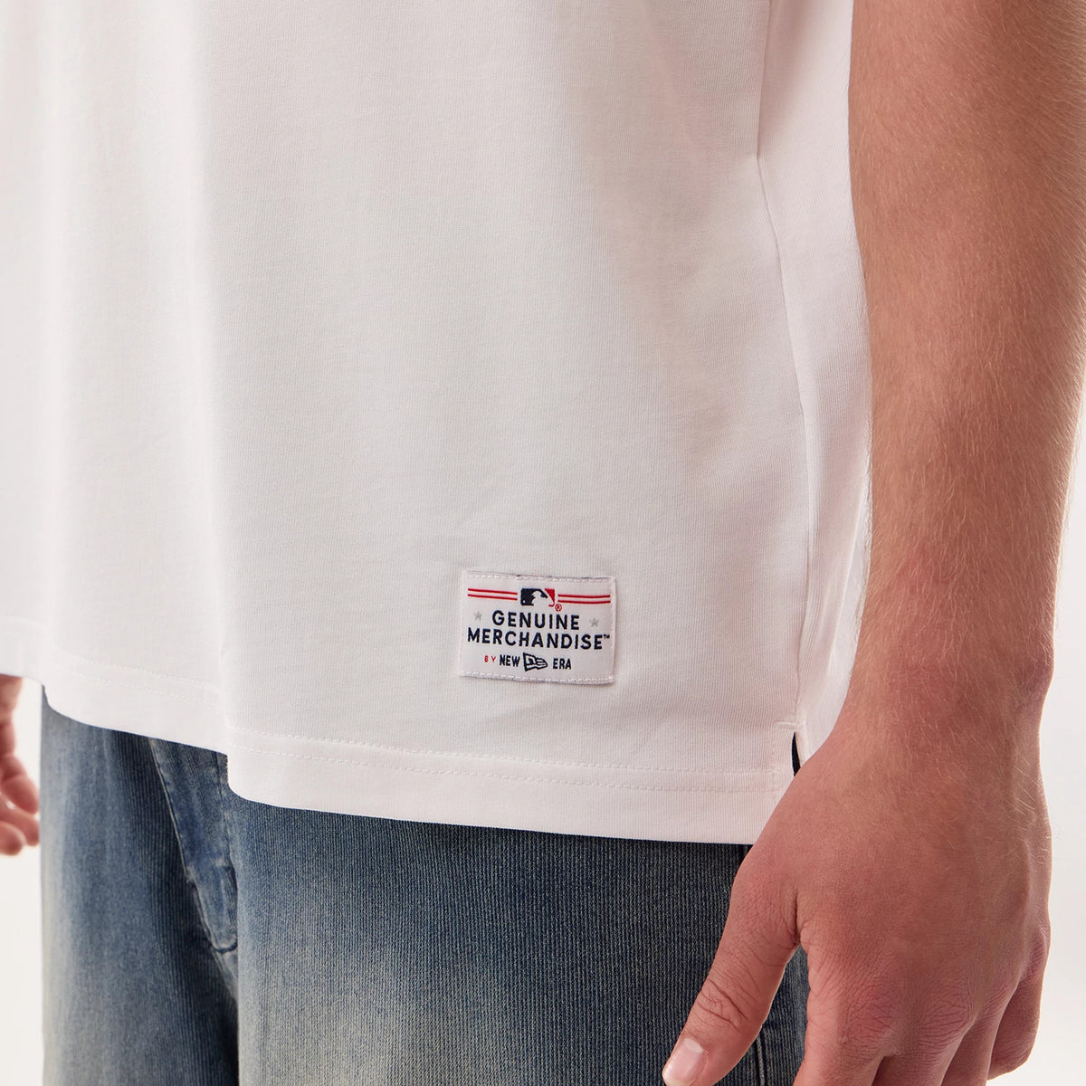 Los Angeles Dodgers MLB Fan Family White Jersey, close-up view on a model showing the MLB Genuine Merchandise patch with New Era logo on the lower front hem of the shirt, styled with blue jeans.