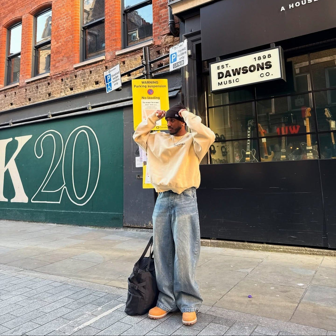 Person standing on a street corner with a building and sign in the background wearing a new era beanie