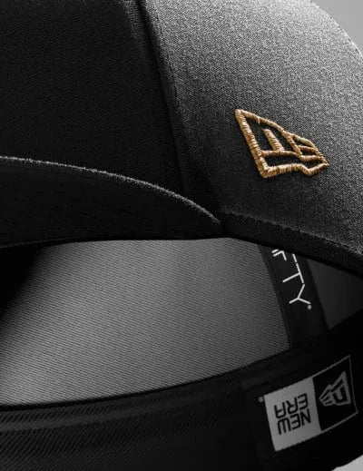 Close-up of a black cap with a gold new era logo on a dark background