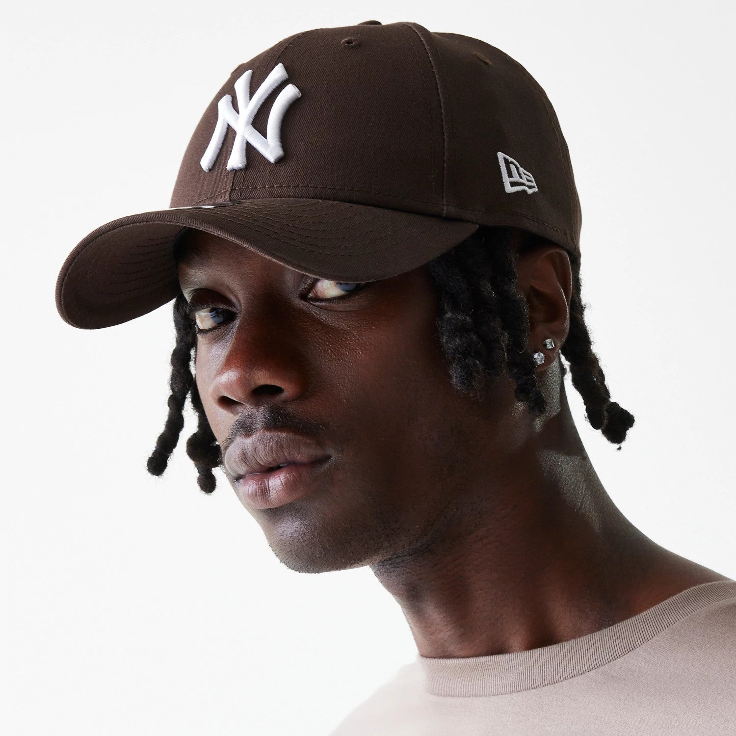New York Yankees League Essential Dark Brown New Era 9FORTY Adjustable Cap, on-model side view showing the white raised embroidered NY logo on the front panel and the New Era flag logo on the left side of the brown structured crown.