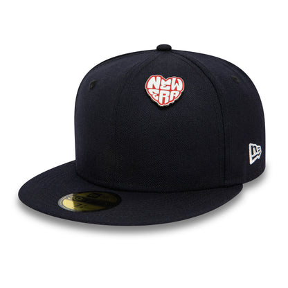New Era Heart Silver Pin Badge, front view showing a black cap with a heart-shaped pin featuring the New Era logo in white at the centre, an embroidered New Era logo on the side and a circular sticker on the brim.