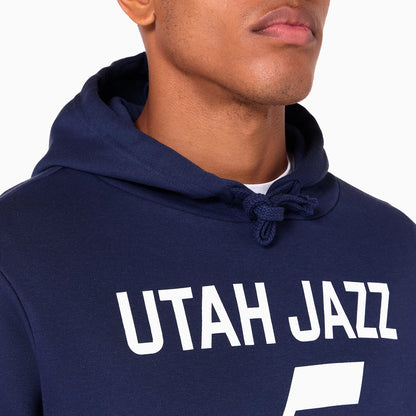 New Era Utah Jazz NBA Navy Pullover Hoodie, front view showing the navy fabric with UTAH JAZZ printed in white across the chest, the hood featuring drawstring ties, and the upper portion of a person's chest and face partially visible.