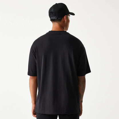 New Era Crest Black Oversized T-Shirt, rear view showing the plain black fabric with a relaxed fit and a rounded neckline, worn by a person also wearing a black cap with a raised New Era logo on the back.