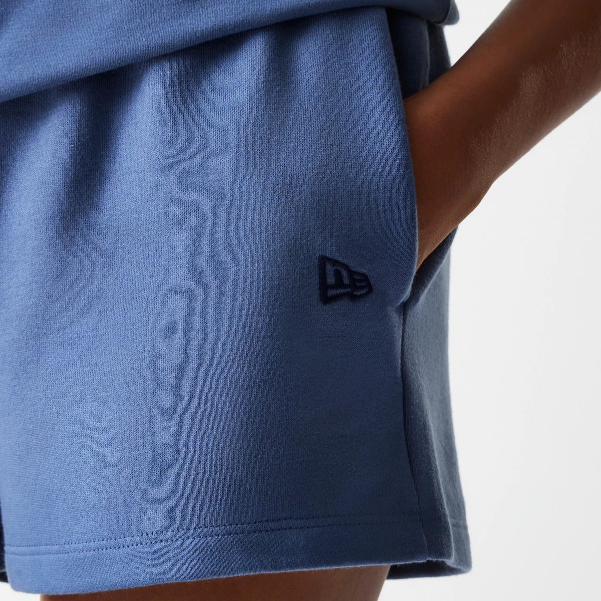 New Era LA Dodgers Womens MLB Midi League Essential Dark Blue Shorts, side view showing the dark blue fabric with a raised New Era logo near the hem above the pocket opening on the right side.