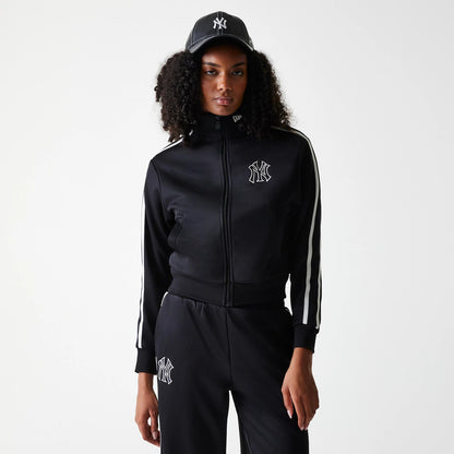 New Era New York Yankees Womens MLB Midi Logo Black Track Jacket, on-model view showing the black track jacket with a front zip and white stripes down the sleeves, the raised Yankees logo on the chest, and a raised New Era logo on a black cap worn.