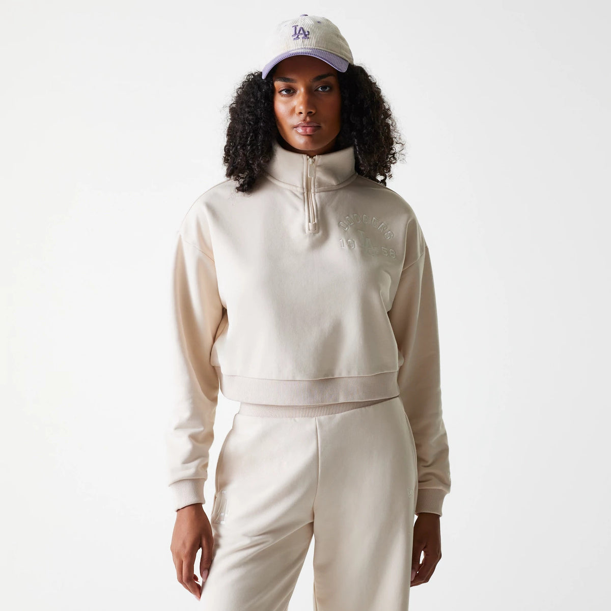 New Era LA Dodgers Womens MLB Tonal Light Beige Cropped 1/4 Zip Sweater, front view on a model wearing a matching cap, highlighting the embossed Dodgers 1958 lettering on the chest and ribbed cuffs.