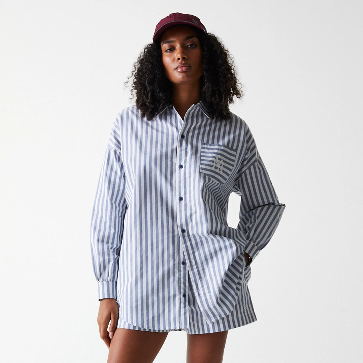 New Era New York Yankees Womens MLB Stripe Dark Blue Long Sleeve Shirt, on a model wearing a burgundy cap, featuring vertical stripes, button-up front, and the distinctive Yankee logo embroidered on the chest pocket.