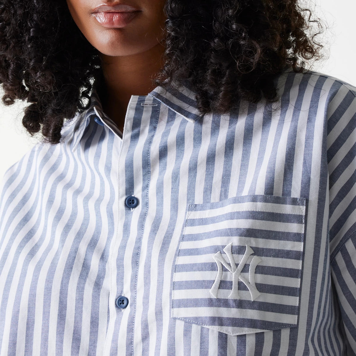 New Era New York Yankees Womens MLB Stripe Dark Blue Long Sleeve Shirt, close-up on a model showing alternating dark blue and white stripes, blue buttons, and the white embroidered NY logo on the left chest pocket.