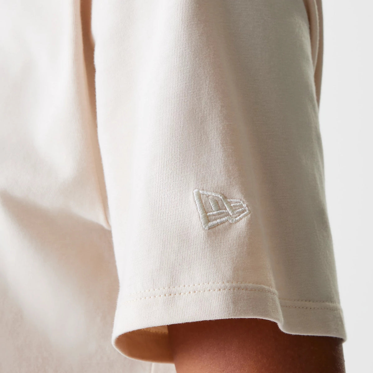 New Era LA Dodgers Womens MLB Tonal Graphic Light Beige Oversized T-Shirt, side view showing the lower half of the sleeve with an embroidered New Era logo in white near the hem on the light beige fabric.