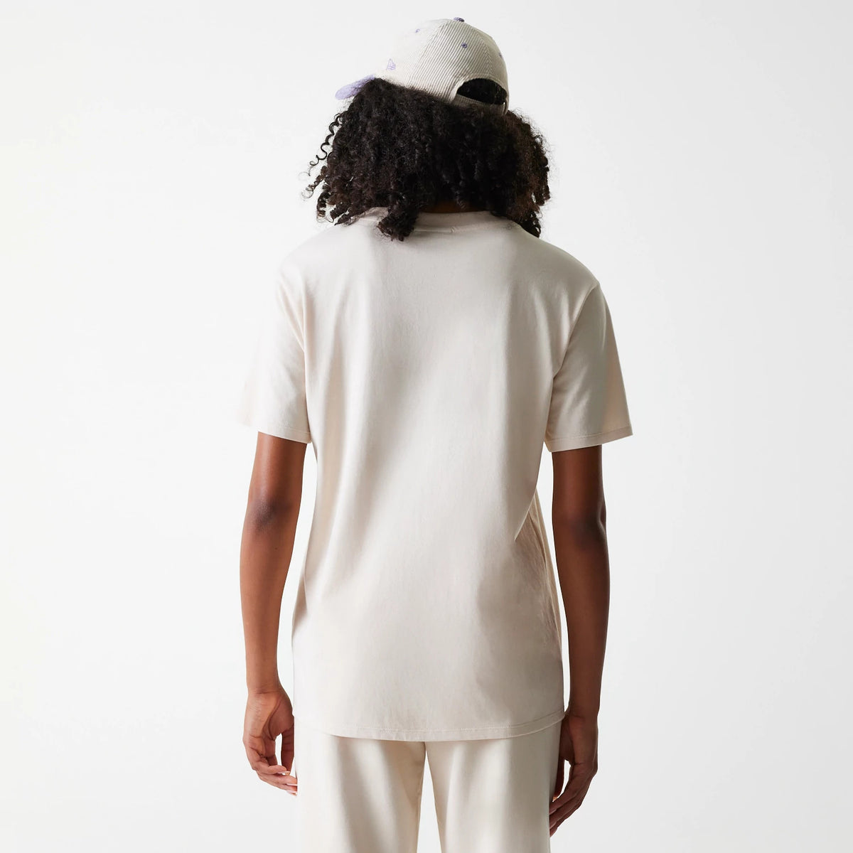New Era LA Dodgers Womens MLB Tonal Graphic Light Beige Oversized T-Shirt, back view showing the plain light beige fabric with short sleeves, on-model with a purple cap displaying an embroidered logo.