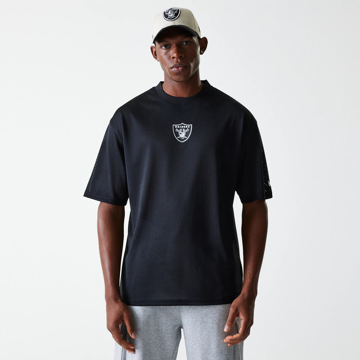 New Era Las Vegas Raiders NFL Essentials Black Oversized Mesh T-Shirt, front view showing a white debossed Raiders logo centred on the chest, short sleeves with a mesh design, worn by a model wearing a grey cap with a raised Raiders logo.
