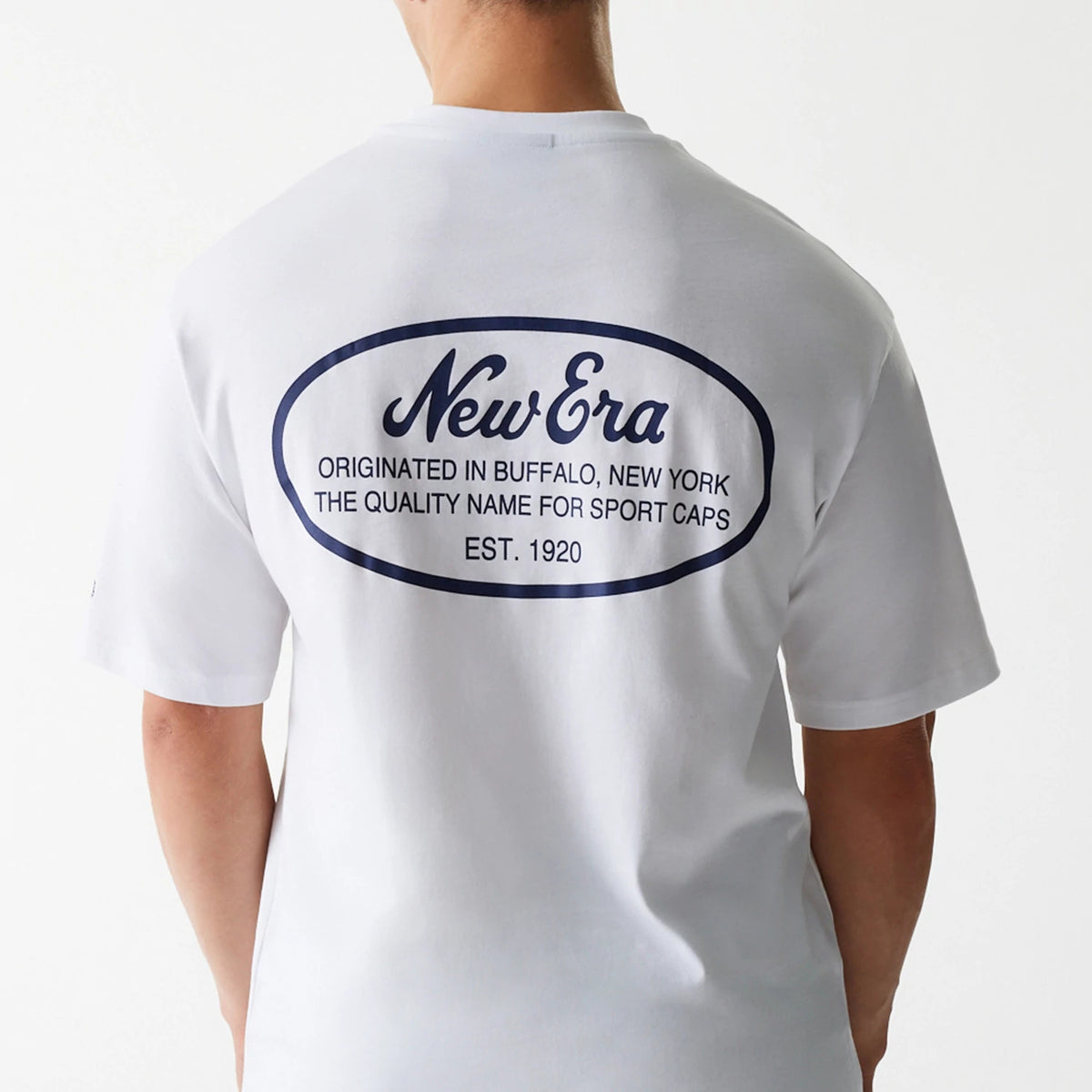 New Era Trucker Patch White Oversized T-Shirt, rear view showing a large blue oval patch with the New Era logo and text detailing the brand's origin on the upper back of the white fabric.