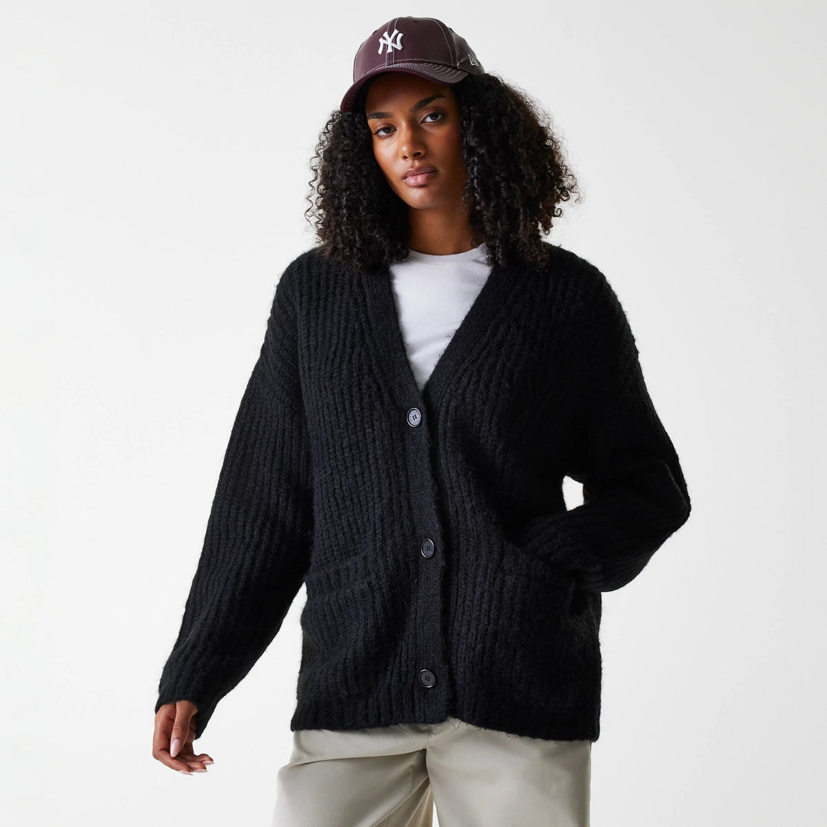 New Era New York Yankees Womens MLB Knit Black Cardigan, on a model styled with a burgundy cap and beige trousers, front view highlighting the button-up design and textured knit pattern of the cardigan.