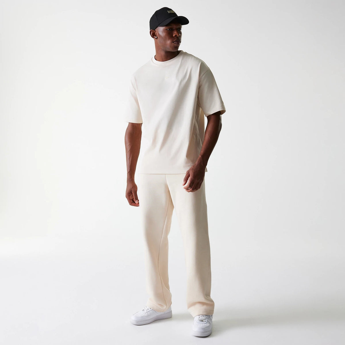 New Era Light Beige Straight Leg Joggers, on-model view with a matching light beige T-shirt, showing the relaxed fit and straight leg cut paired with white trainers and a black cap.