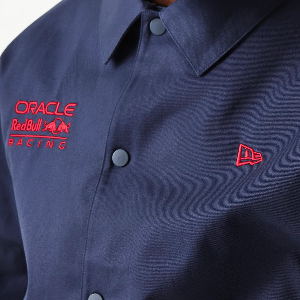 New Era Red Bull Racing Dark Blue Oversized Coach Jacket, front view showing the buttoned front with red Oracle Red Bull Racing embroidery on the left chest and a raised red New Era logo on the right chest.