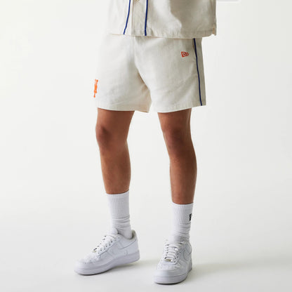 New Era New York Mets MLB Piping Open Cream Shorts, front three-quarter view showing the cream shorts with orange Mets logo on the lower right leg, side blue piping, and a red embroidered New Era logo above the hem.