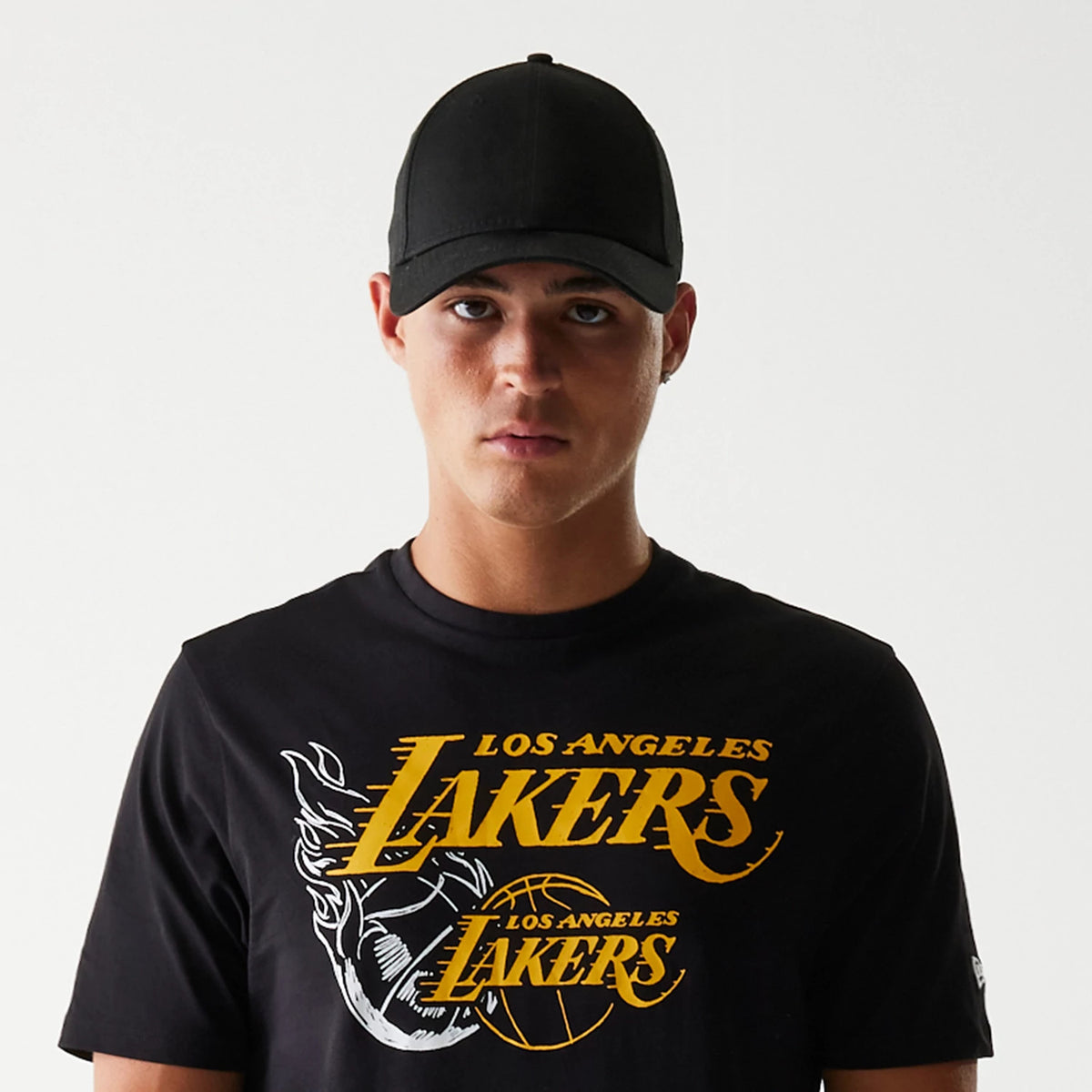 New Era LA Lakers NBA Flame Graphic Black T-Shirt, front view showing yellow Los Angeles Lakers text across the chest with a flame graphic beneath, worn by a model with a plain black cap.