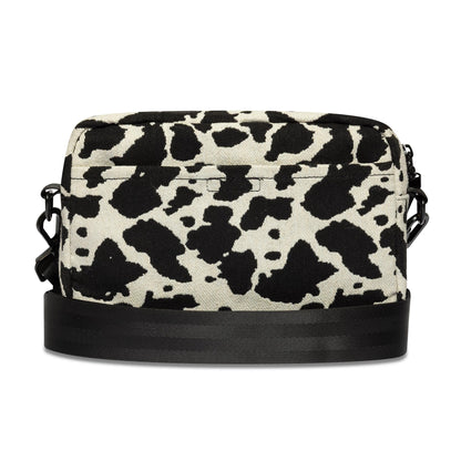 New Era Cow Jacquard Light Beige Waist Bag, front view showing a light beige and black cow print pattern across the rectangular shape, with a black zip closure along the top and an attached adjustable black strap at the sides.