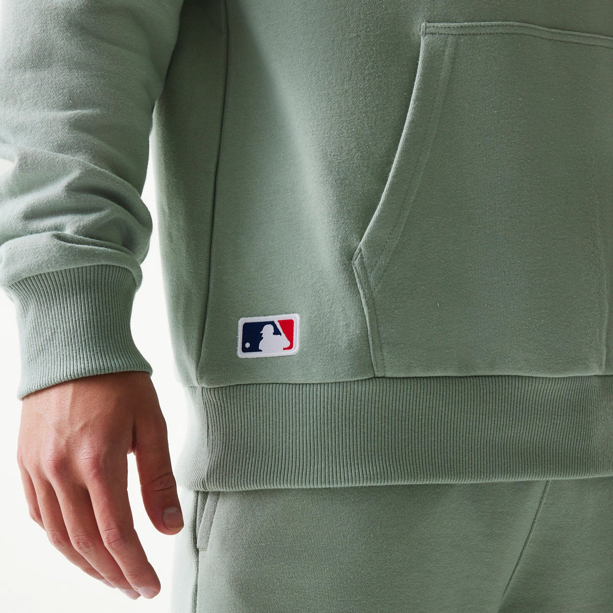 New Era LA Dodgers MLB Midi Pastel Green Oversized Pullover Hoodie, side view showing a small embroidered MLB logo near the bottom hem, a large kangaroo pocket, and ribbed cuffs, styled with matching joggers.