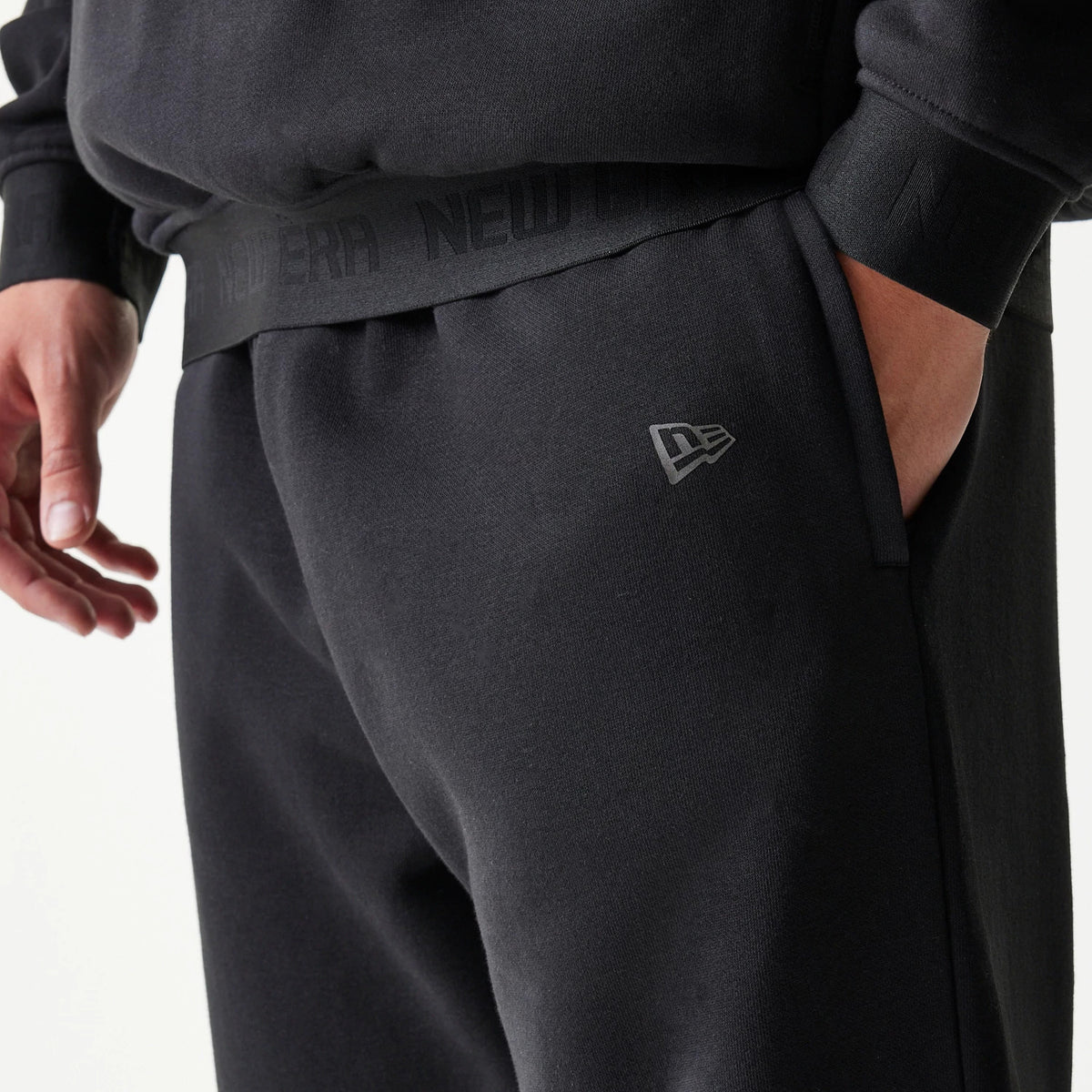 New Era Tech Black on Black Straight Leg Joggers, close-up view showing the black New Era flag logo on the right thigh, with a black elastic waistband featuring discreet New Era branding.