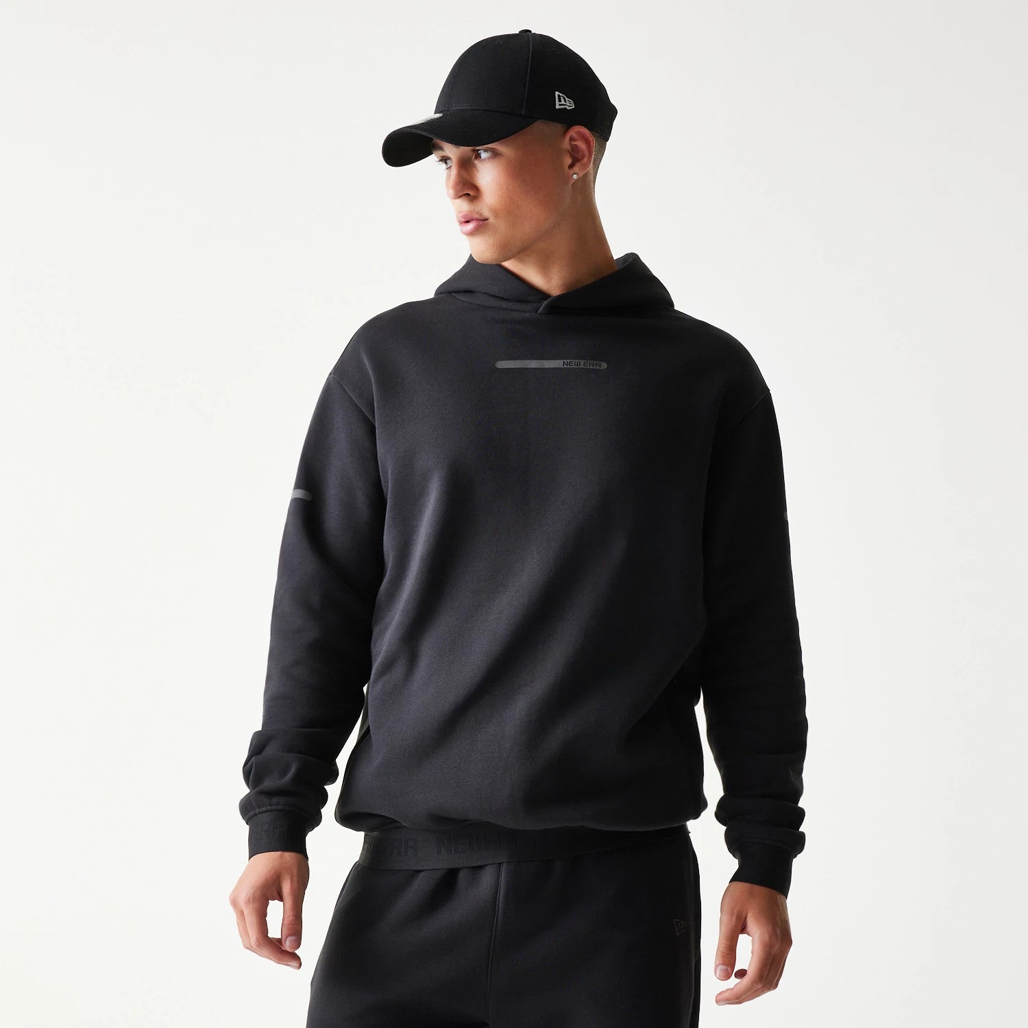 The model is wearing this New Era Tech Strip Oversized Pullover Hoodie in black. 3