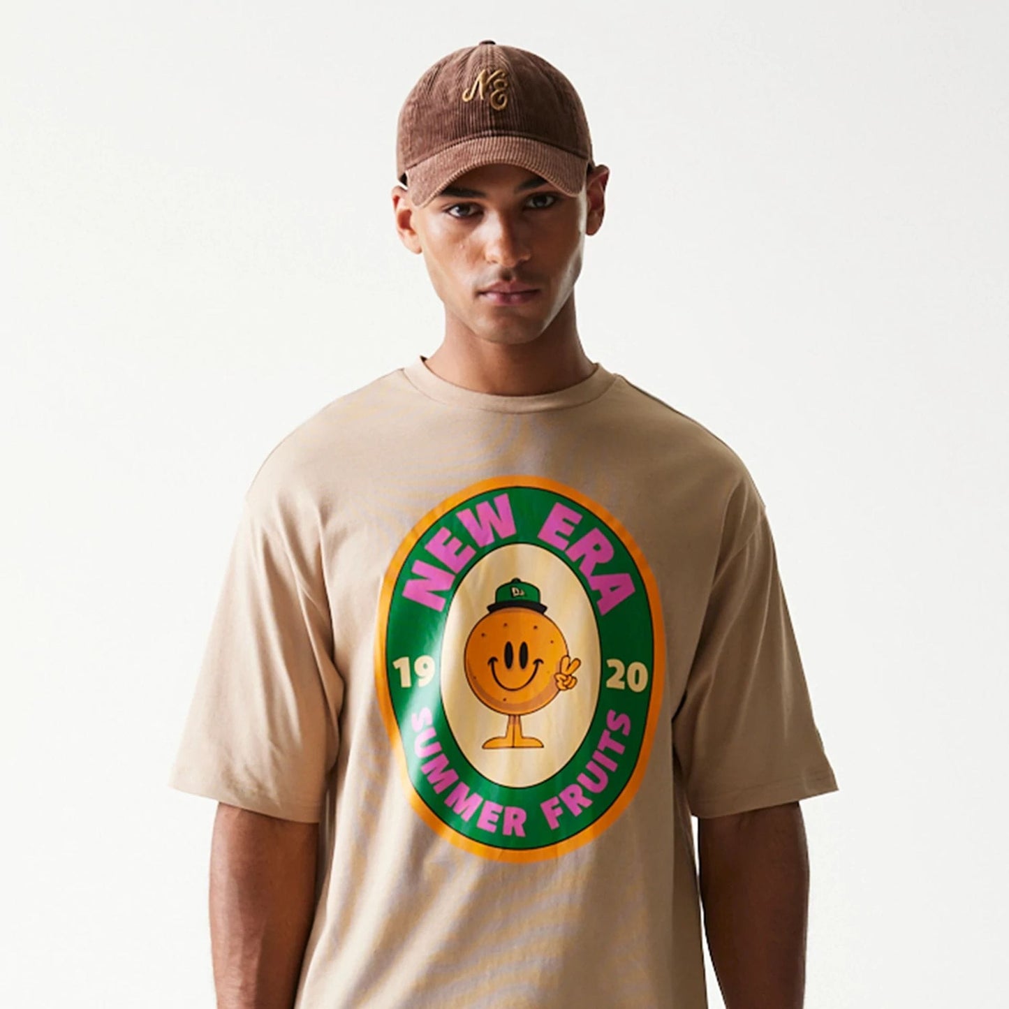 The model is wearing this New Era Orange Fruit Graphic Oversized T-Shirt in light beige. 3