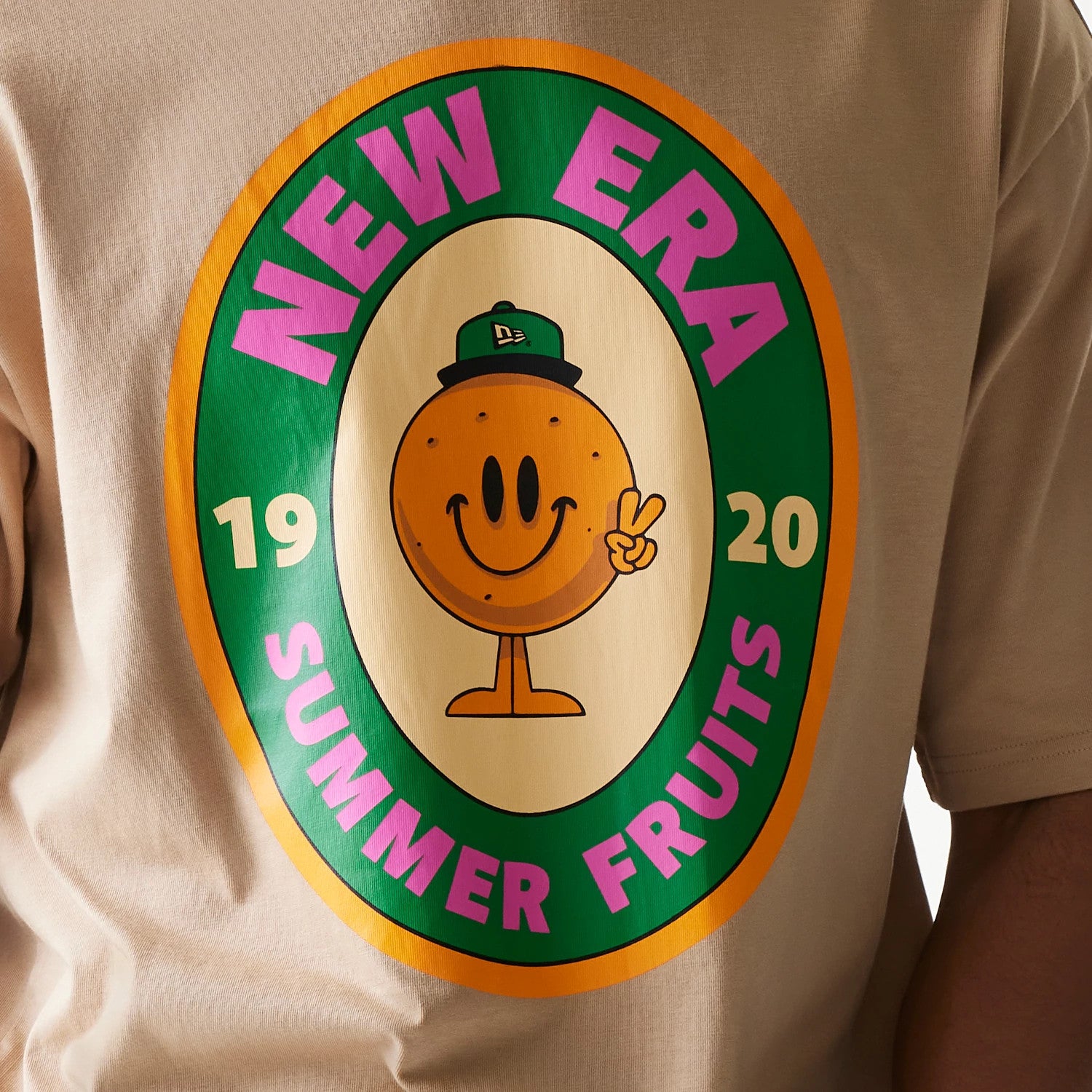 The model is wearing this New Era Orange Fruit Graphic Oversized T-Shirt in light beige. 6