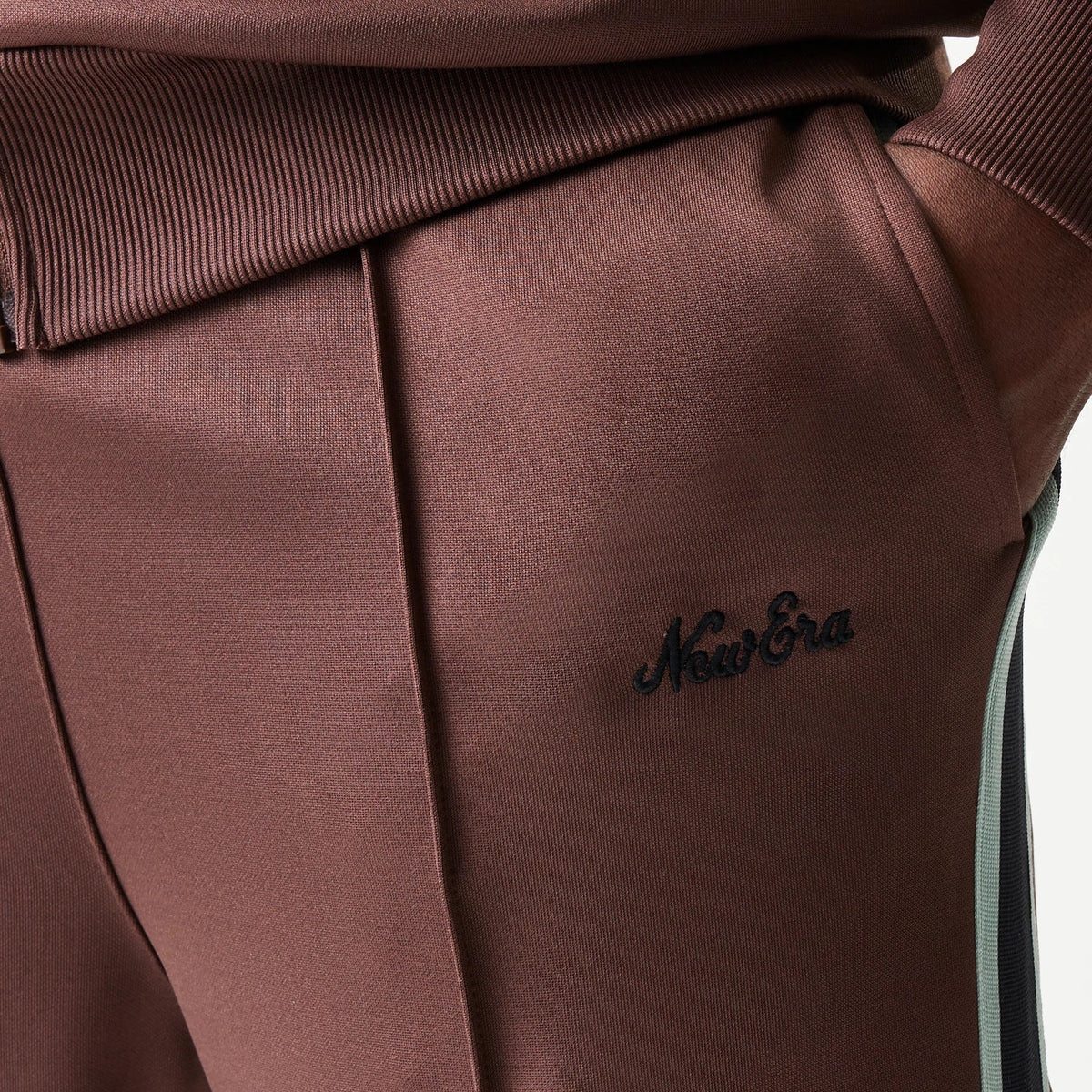 New Era Script Brown Straight Leg Joggers, close-up showing the black embroidered New Era script logo on the brown fabric above the front pocket, with contrasting side stripe running down the leg.