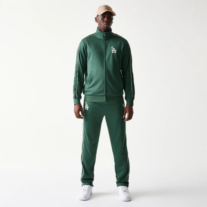 New Era LA Dodgers MLB Piping Dark Green Straight Leg Joggers, front view on a model with an LA Dodgers cap and matching jacket, showing the white embroidered LA logo on the left thigh and piping detail along the sides.