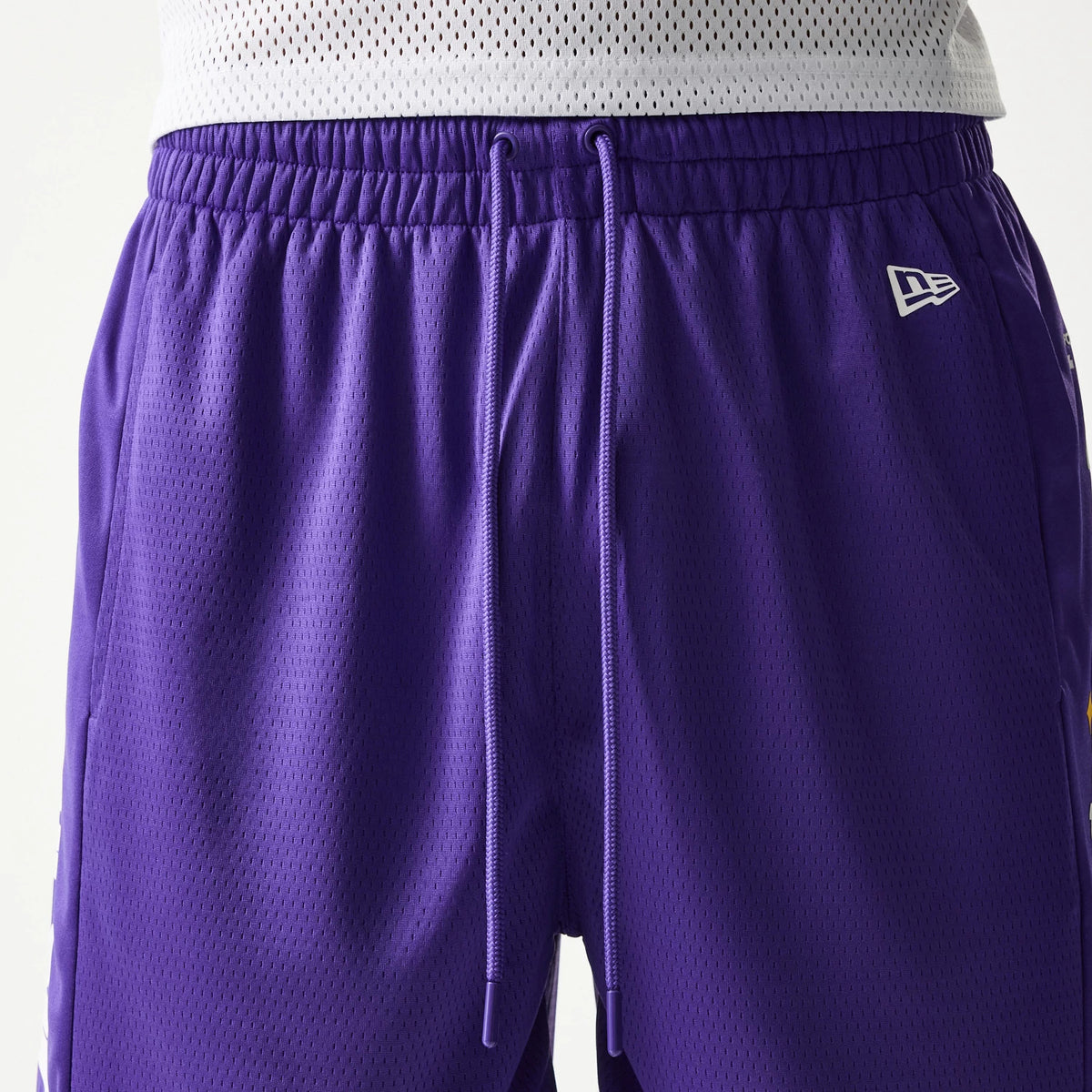 New Era LA Lakers NBA Mesh Purple Shorts, front view showing wide elastic waistband with drawstrings, a white embroidered New Era logo on the upper left leg, and detailed mesh texture throughout the purple fabric.
