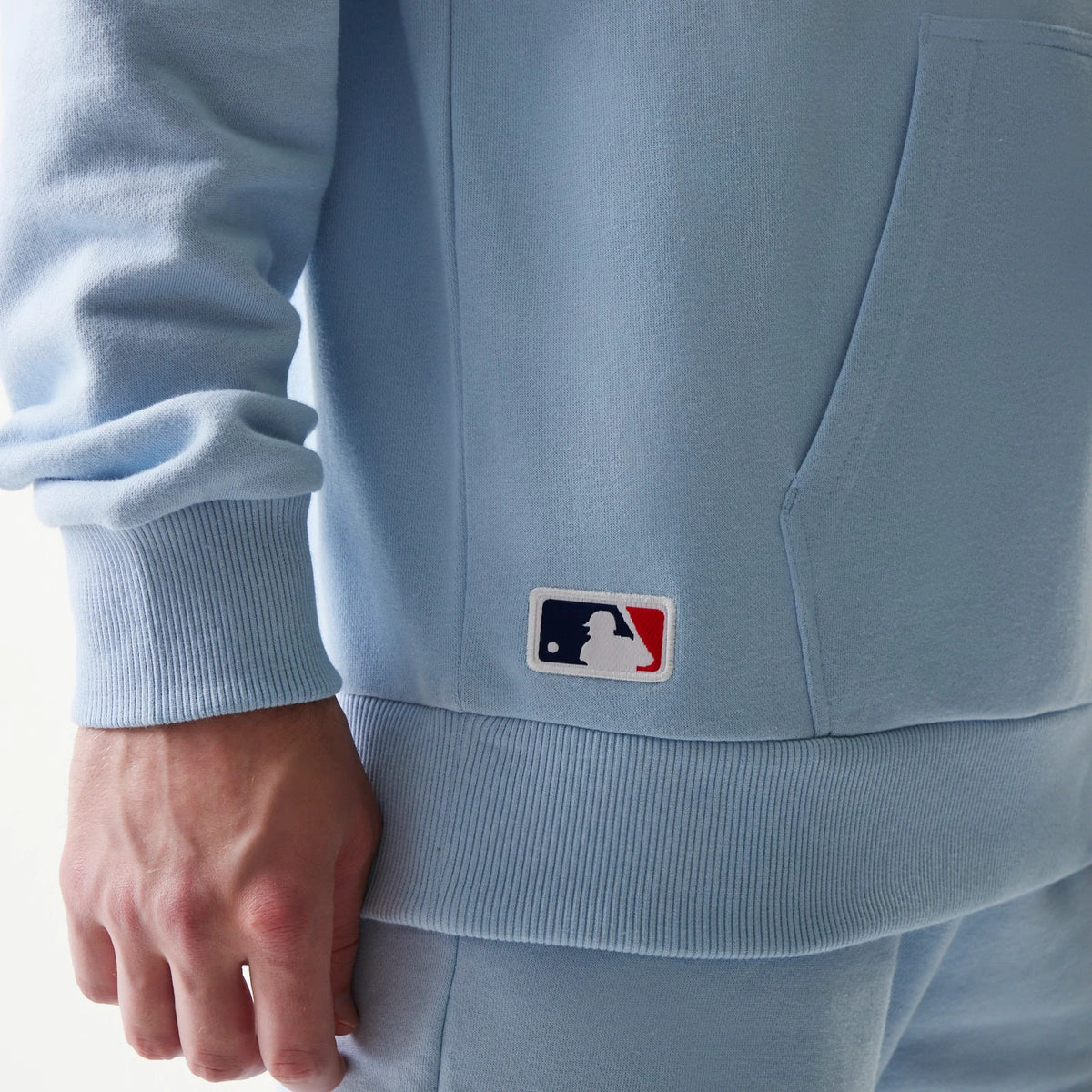 New Era New York Yankees MLB Midi Pastel Blue Oversized Pullover Hoodie, side view showing an embroidered MLB logo near the hem, a large pocket on the front and ribbed cuffs, on-model styled with matching blue bottoms.