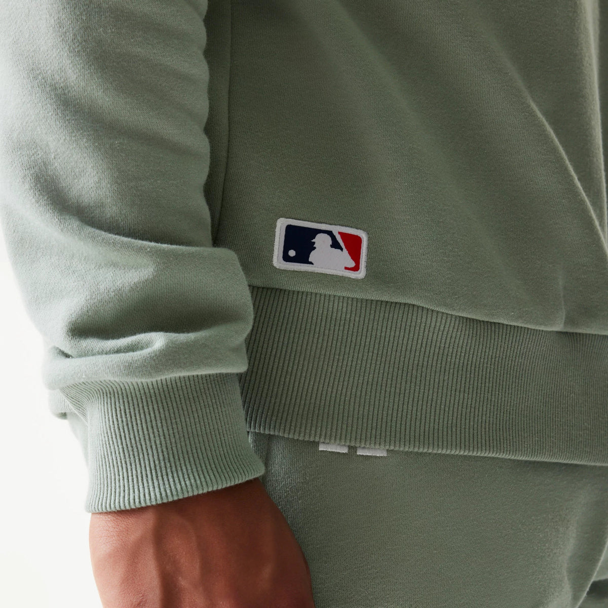 New Era LA Dodgers MLB Midi Green Oversized Crew Neck Sweater, close-up view showing the embroidered MLB logo on the lower left side, with ribbed cuffs and hem in a soft green fabric.