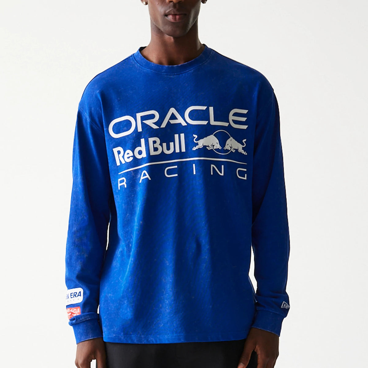 New Era Red Bull Racing Linear Graphic Blue Long Sleeve T-Shirt, front view showing a white printed logo with Oracle, Red Bull and Racing text across the chest, worn by a model with New Era and partner branding on the sleeves.