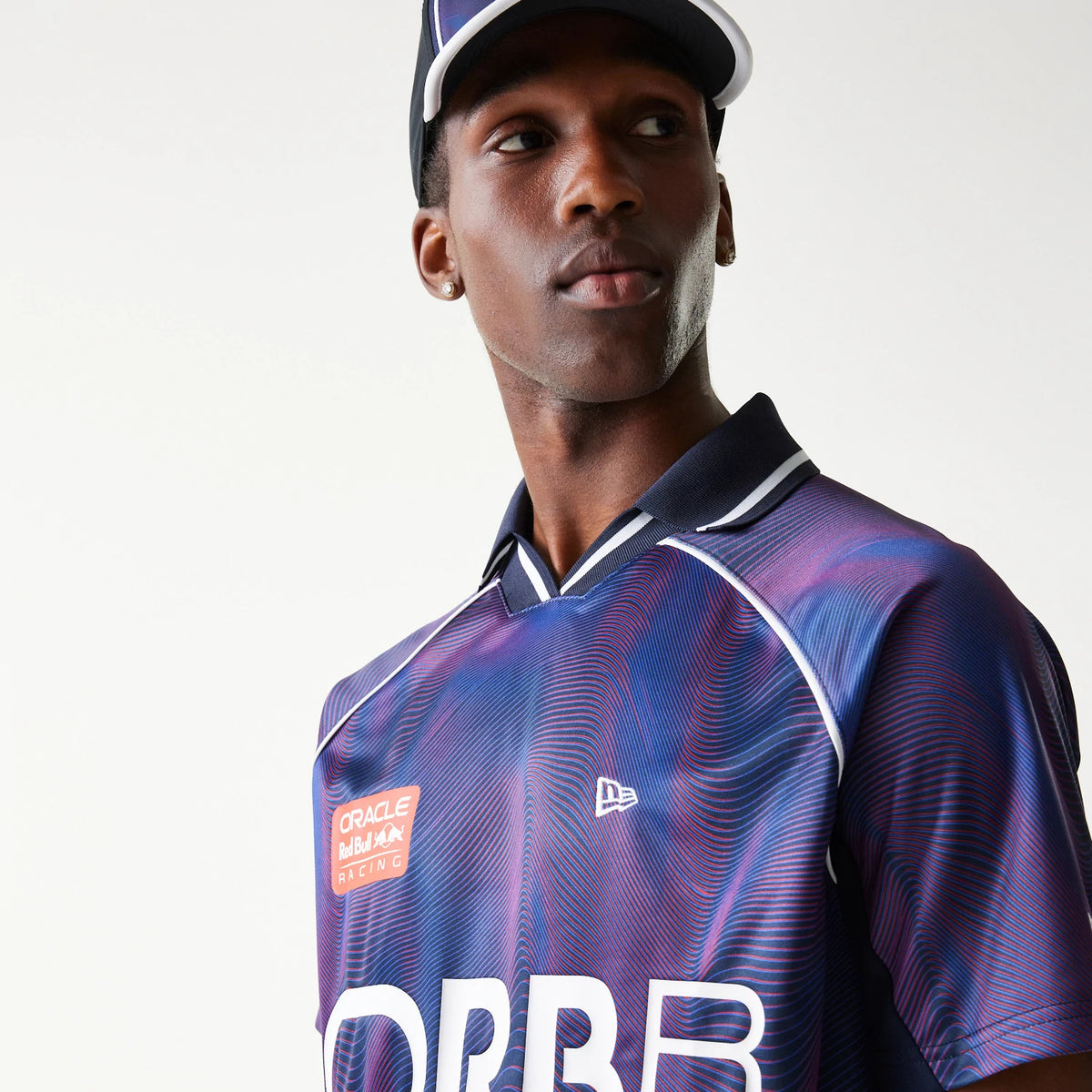 New Era Red Bull Racing All Over Print Dark Blue Football T-Shirt, front view on-model showcasing a large ORBR graphic, an embroidered New Era logo on the chest, and a patterned design with a contrasting dark collar and sleeves.