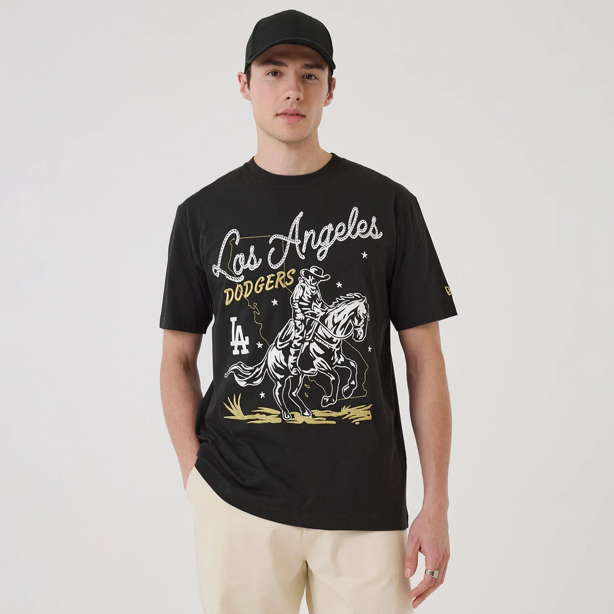 New Era LA Dodgers MLB Cowboy Graphic Black T-Shirt, front view on-model showing a graphic of a cowboy on horseback with Los Angeles Dodgers text, LA logo, and intricate star details in white and gold across the chest.
