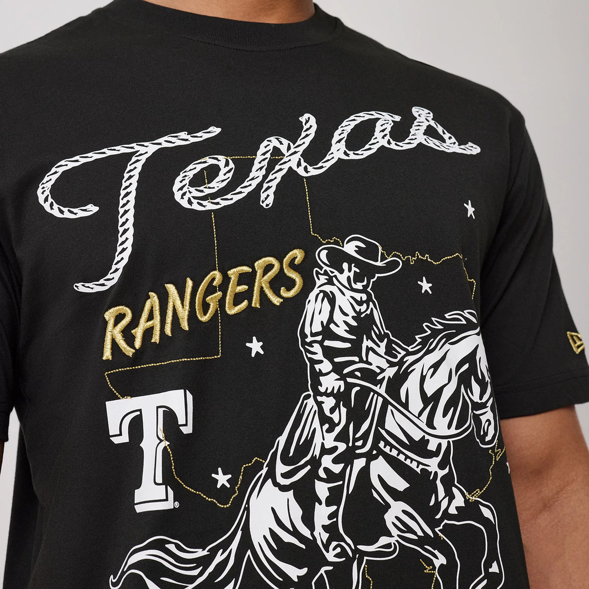 New Era Texas Rangers MLB Cowboy Graphic Black T-Shirt, front view showcasing a graphic of a cowboy on horseback in white and gold, with embroidered Texas Rangers lettering across the chest and a small embroidered New Era logo on the sleeve.