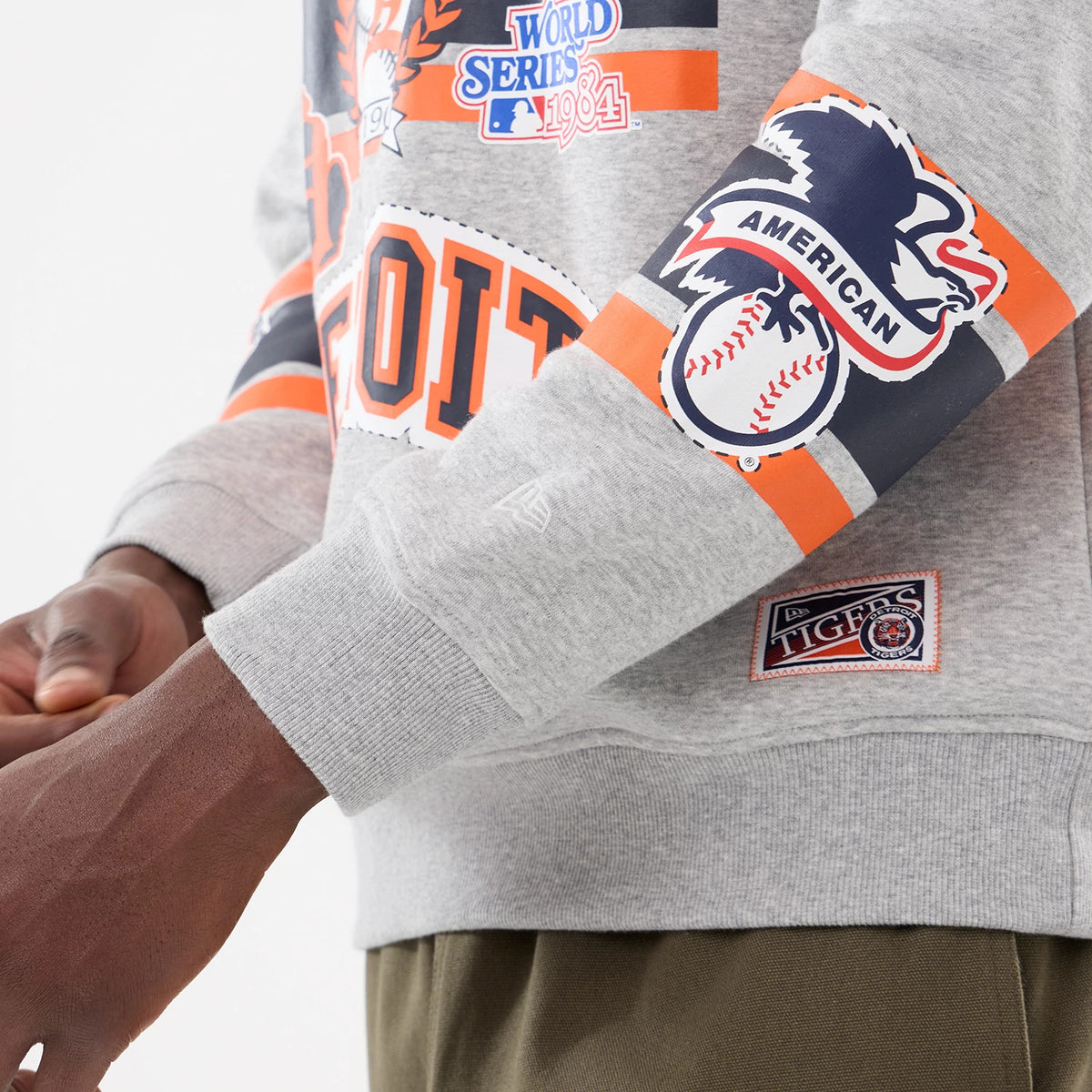 New Era Detroit Tigers MLB Sport Classic Grey Crew Neck Sweater, side view showing the Detroit lettering across the chest, American logo on the sleeve, and a Tigers patch near the hem, with a relaxed fit.