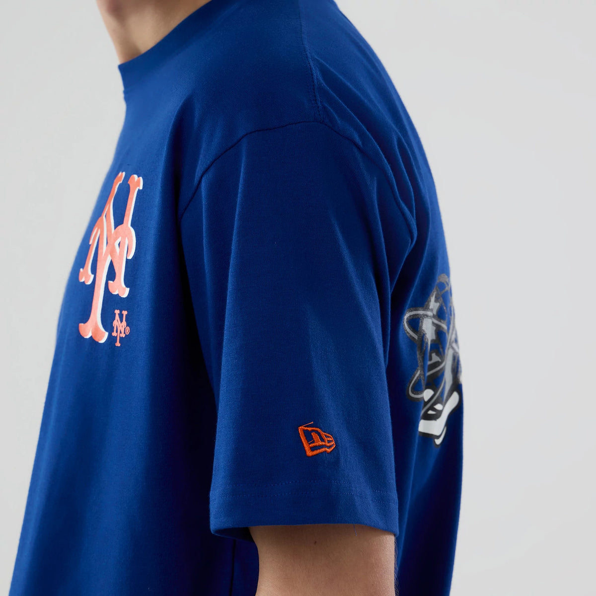 New Era New York Mets MLB Graphic Blue T-Shirt, side view showing the large orange Mets logo printed on the chest, detailed graphics on the side, and an embroidered orange New Era logo on the sleeve.