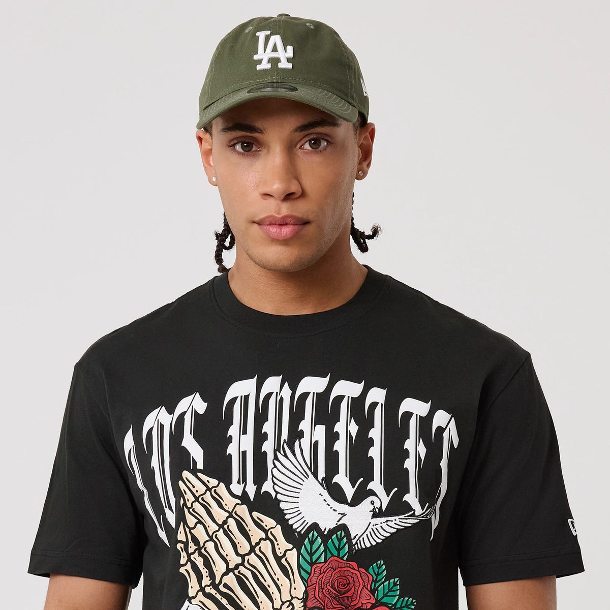 New Era LA Dodgers MLB Script Graphic Black T-Shirt, front view on-model featuring Los Angeles lettering and a detailed graphic of praying hands and a dove, with the New Era logo embroidered on the sleeve.