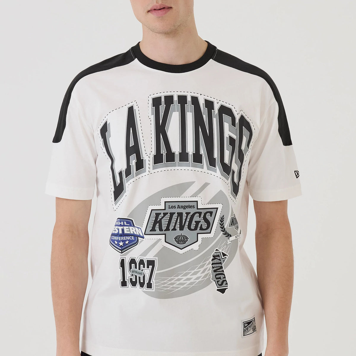 New Era LA Kings NHL Sport Classic White T-Shirt, front view on-model featuring LA KINGS text across the chest, multiple graphic patches including Los Angeles Kings and NHL Western Conference logos, and a small embroidered New Era logo on the sleeve.