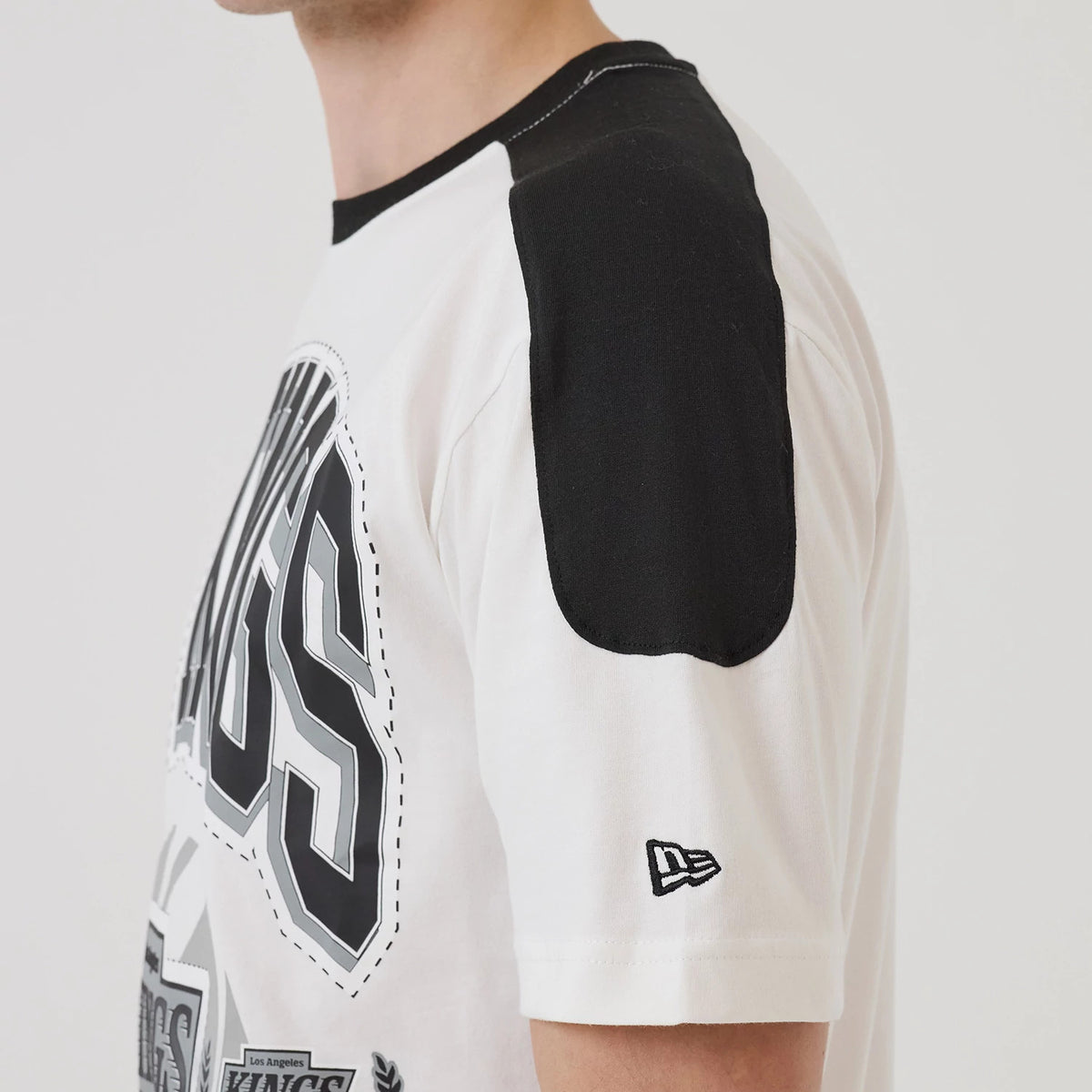 New Era LA Kings NHL Sport Classic White T-Shirt, three-quarter view showcasing a Kings graphic in black and grey on the front, black shoulder panels, and an embroidered New Era logo on the left sleeve near the cuff.
