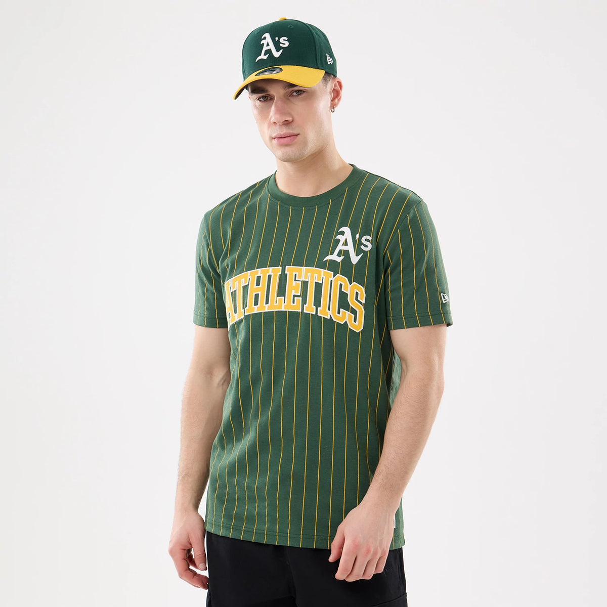 New Era Athletics MLB Pinstripe Dark Green T-Shirt, front view on-model showing the yellow pinstripes on a dark green base, white embroidered A's logo on the chest, and large yellow ATHLETICS lettering across the front.