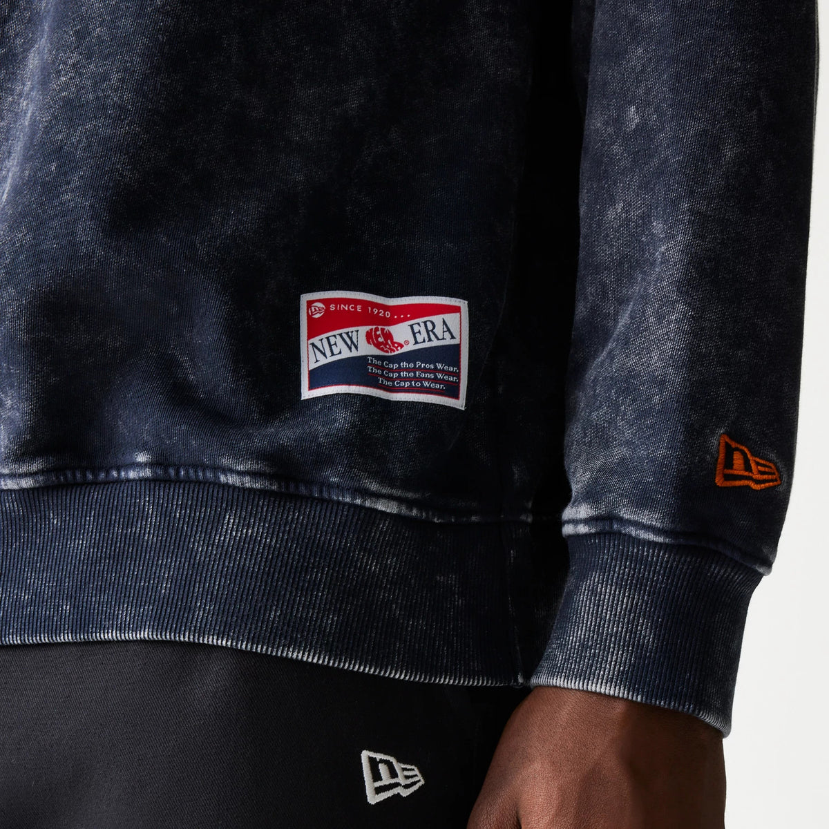 New Era Chicago Bears NFL Navy Crew Neck Sweater, close-up view showing the New Era patch above the ribbed hem and the orange embroidered New Era flag logo on the left cuff, with a washed navy texture.